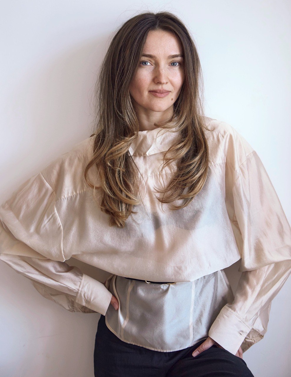 Woman in a cream blouse standing against a white wall
