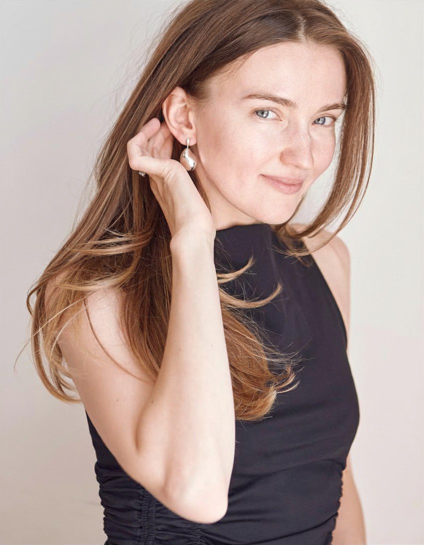 Alina in a black top, smiling, tucking her hair behind her ear
